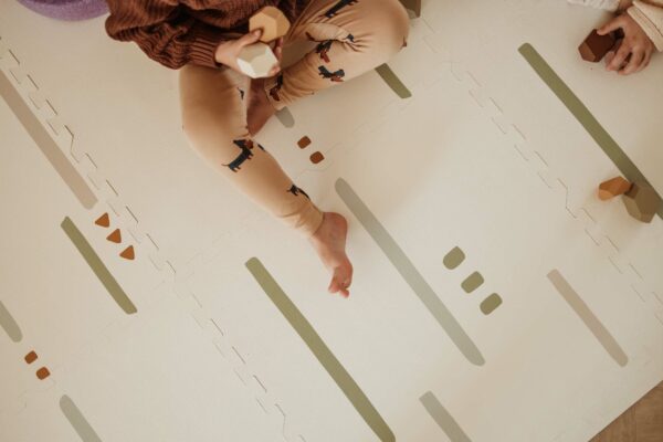 PlanandGo_EEVAA_farm_puzzlemat_backside_stripes_and_icons_child_is_sitting_on_the_mat Play&Go 3u1 EEVAA dvostrana podloga za igru – Farma (120x180cm) - Image 4