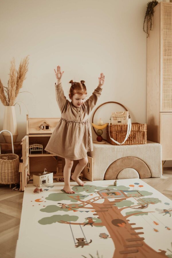 PlayandGo_EEVAA_treehouse_puzzlemat_child_is_standing_on_the_mat_with_raised_arms Play&Go 3u1 EEVAA dvostrana podloga za igru – Kućica na drvetu/Zvjezdice (120x180cm) - Image 15