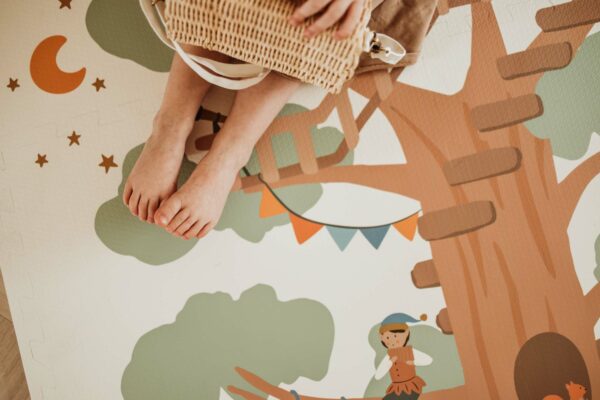 PlayandGo_EEVAA_treehouse_puzzlemat_child_sitting_on_the_mat_with_basket_moon_stars_and_elf Play&Go 3u1 EEVAA dvostrana podloga za igru – Kućica na drvetu/Zvjezdice (120x180cm) - Image 7